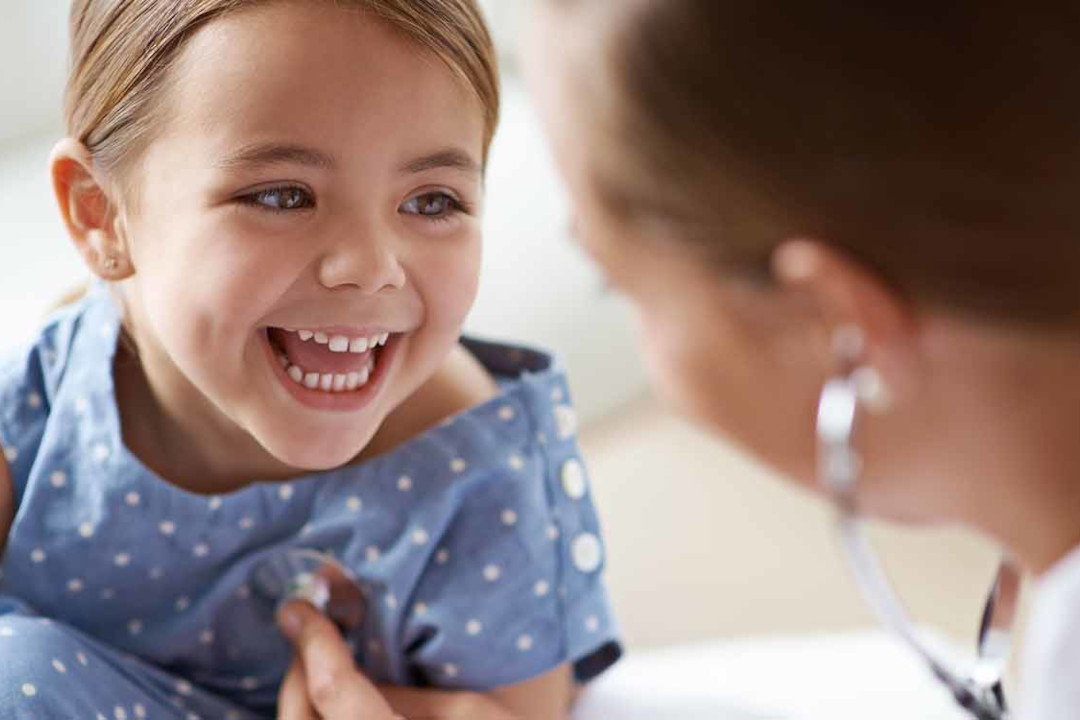 Eine Ärztin prüft den Herzschlag eines lachenden Mädchens mit einem Stethoskop.