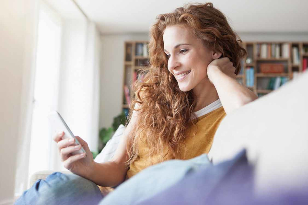 Eine Frau sitzt auf ihrem Sofa mit dem Handy in der Hand