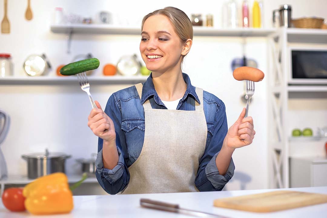 Frau hält 2 Gabeln in der Hand mit einer Wurst und einer Gurke