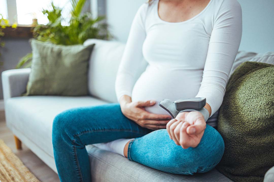 Schwangere Frau sitzt mit einem Blutdruckmessgerät auf dem Sofa