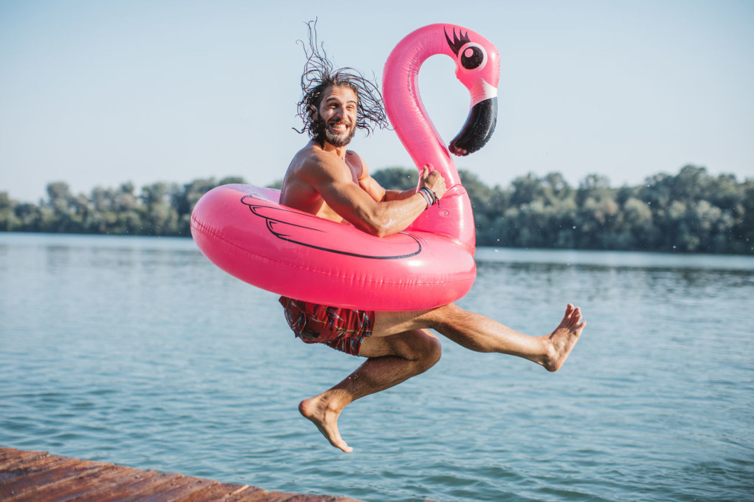 Ein Mann der einen Pinken Flamingo-Schwimmring trägt und in den See hüpft