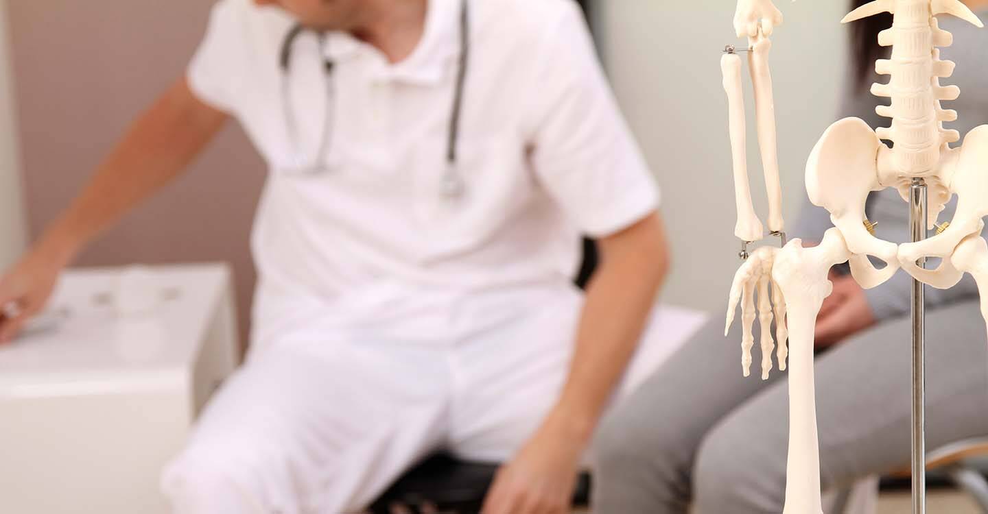 Arzt mit Patientin und einem Skelett im Untersuchungszimmer