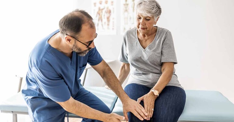 Arzt spricht mit einer Patientin, die auf einem Behandlungstisch sitzt