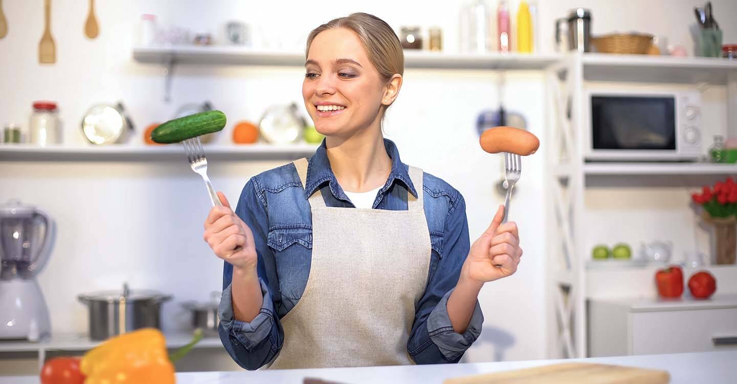 Frau hält 2 Gabeln in der Hand mit einer Wurst und einer Gurke