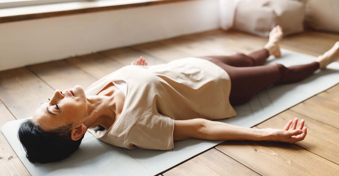 Yoga: Frau liegt mit geschlossenen Augen auf einer Matte