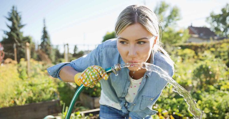 Frau trinkt aus einem Gartenschlauch