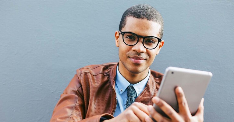 Junger Mann mit Smartphone in der Hand, schaut in die Kamera