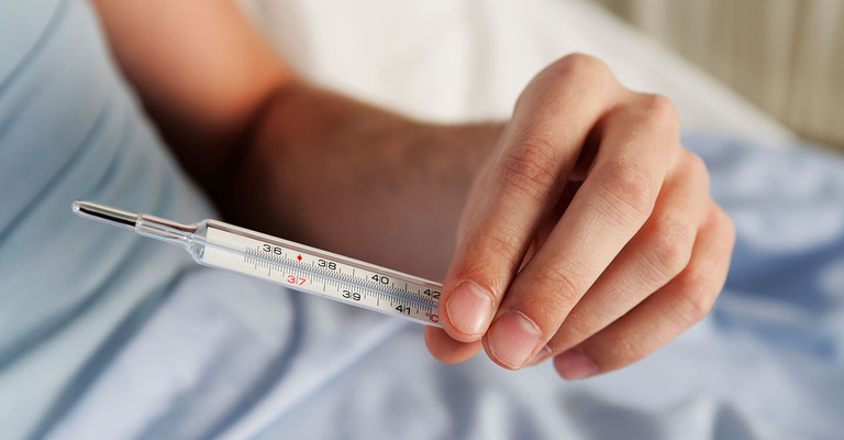 Mann hält ein Fieberthermometer in der Hand