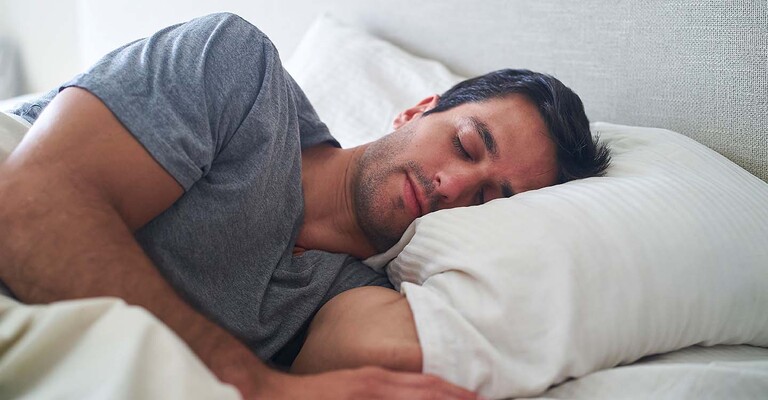 Mann liegt schlafend auf der Seite im Bett