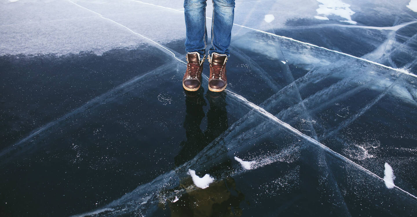 Es sind Füße einer Person zu sehen, die auf einer dicken Eisschicht steht.