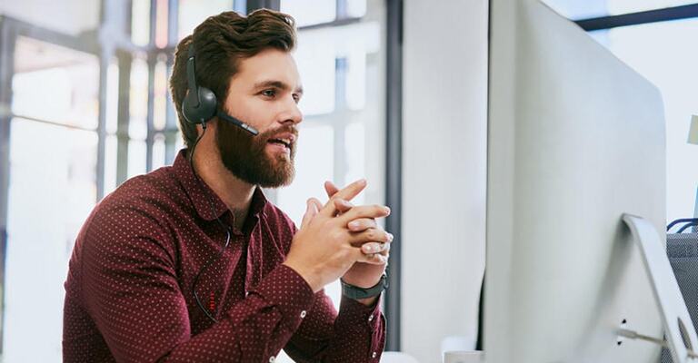 Servicemitarbeiter telefoniert mit einem Headset und schaut auf seinen Bildschirm.