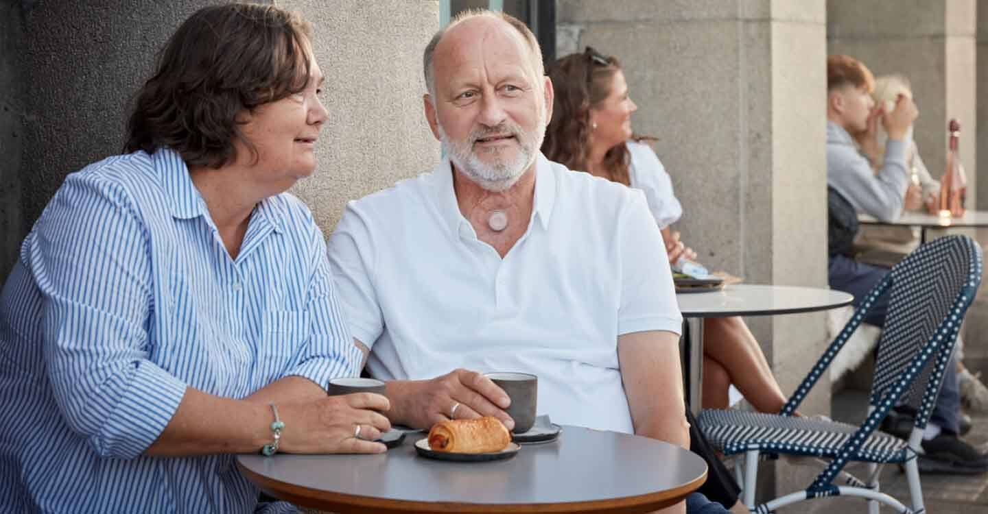 Ehepaar sitzt draußen an einem kleinen Tisch und trinkt Kaffee.