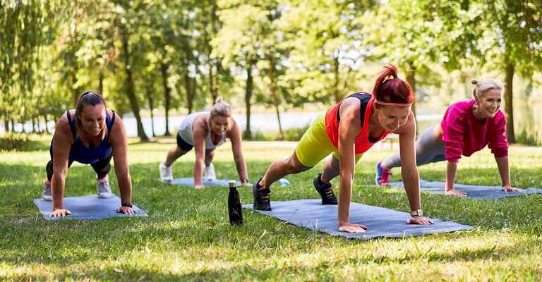 Vier Frauen in Sportbekleidung machen  im Park Liegestuetzen auf Sportmatten