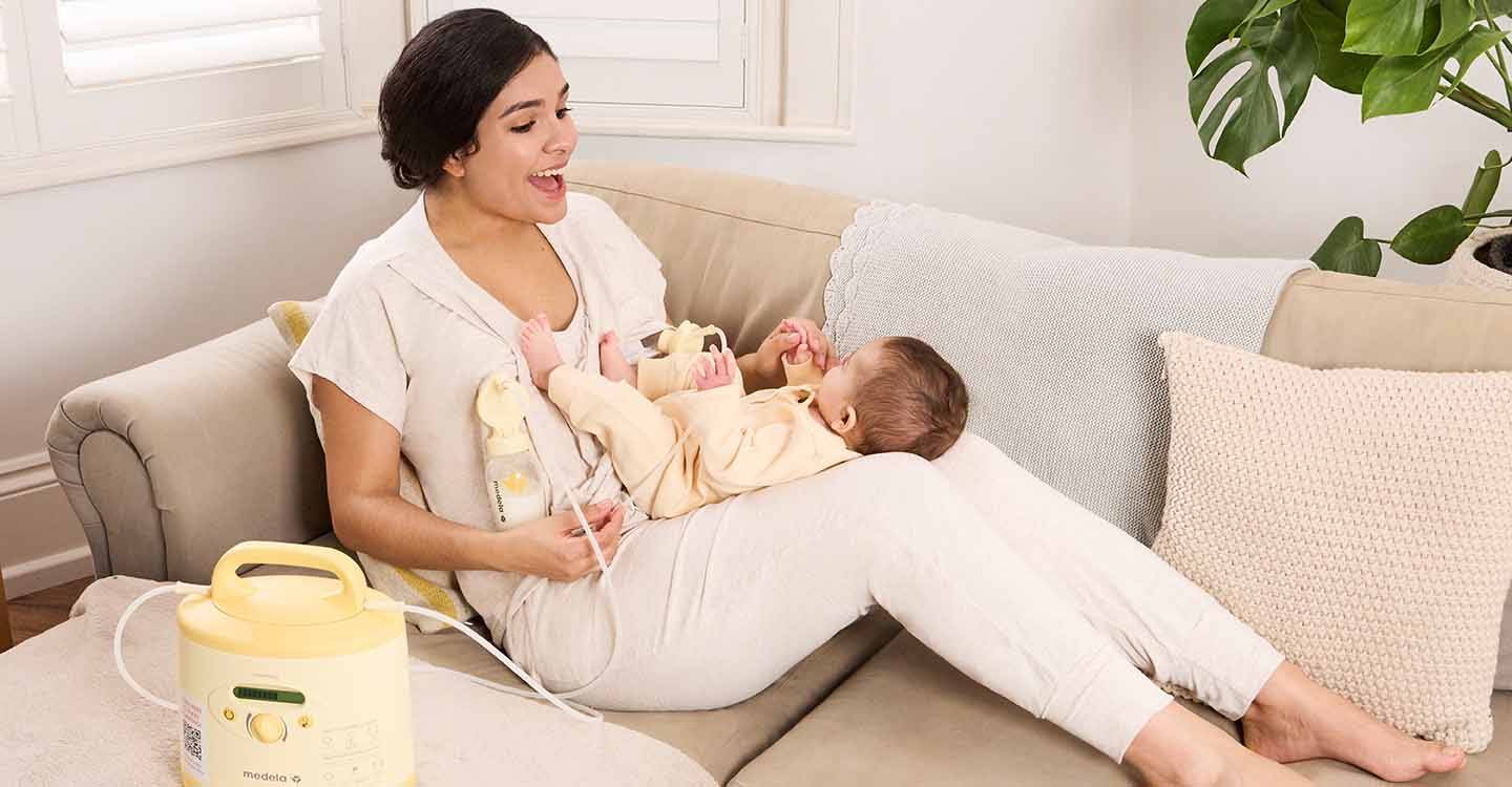 Eine Frau sitzt mit ihrem Baby auf dem Schoß auf dem Sofa und pumpt ihre Milch ab.