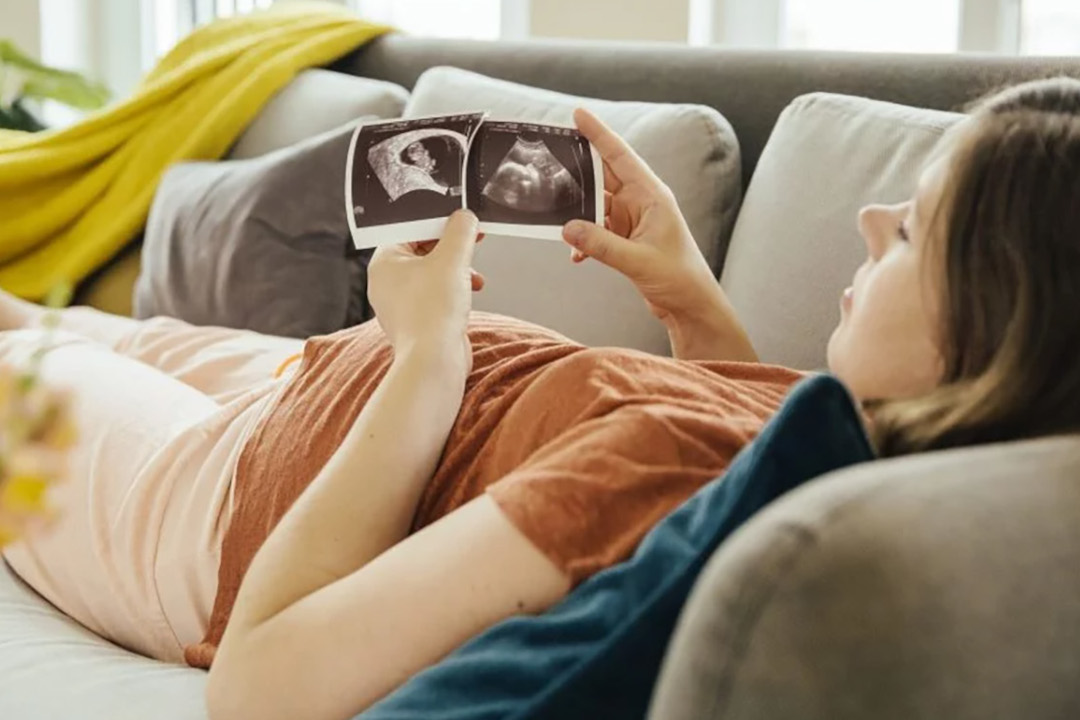 Eine Frau liegt auf dem Sofa und betrachtet zwei Ultraschallbilder.