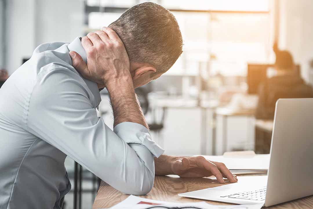 Mann am Tisch stützt seinen schmerzenden Nacken